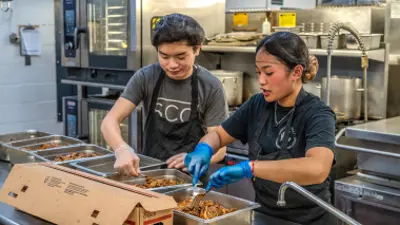 Two students preparing food in a kitchen.