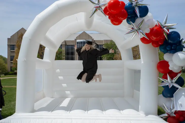 a student wearing a cap and gown jumping in a bounce house