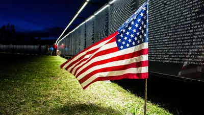 An American flag flies in front of the Wall That Heals at nighttime