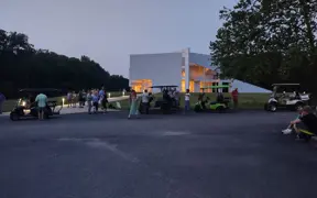 Visitors gathering near the building and parked golf carts in a paved area.