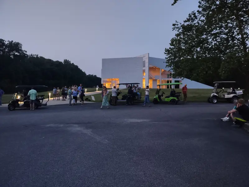 Visitors gathering near the building and parked golf carts in a paved area.