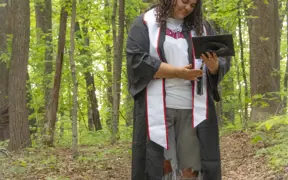 A 2025 graduate stands on USI's Bent Twig Trail 