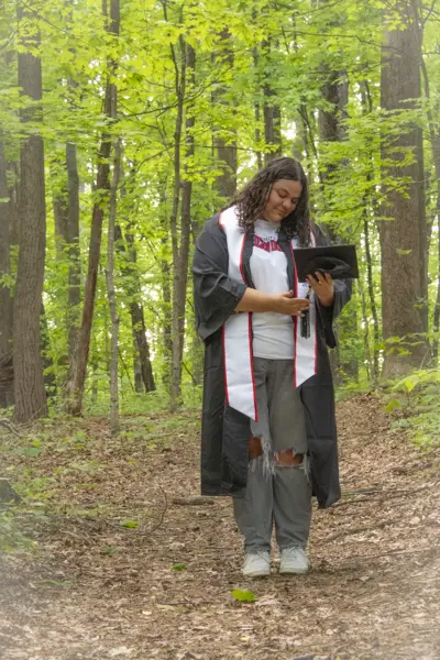 A 2025 graduate stands on USI's Bent Twig Trail 