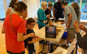 People interacting at a craft table with supplies and materials arranged across the surface.