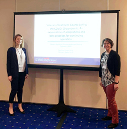 Drs. Stacer and Jalain standing with a projector screen with presentation title