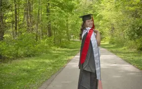 A 2025 graduate looks over her shoulder, her gown and honors stole thrown over her shoulder on the paved USI/Burdette Trail 