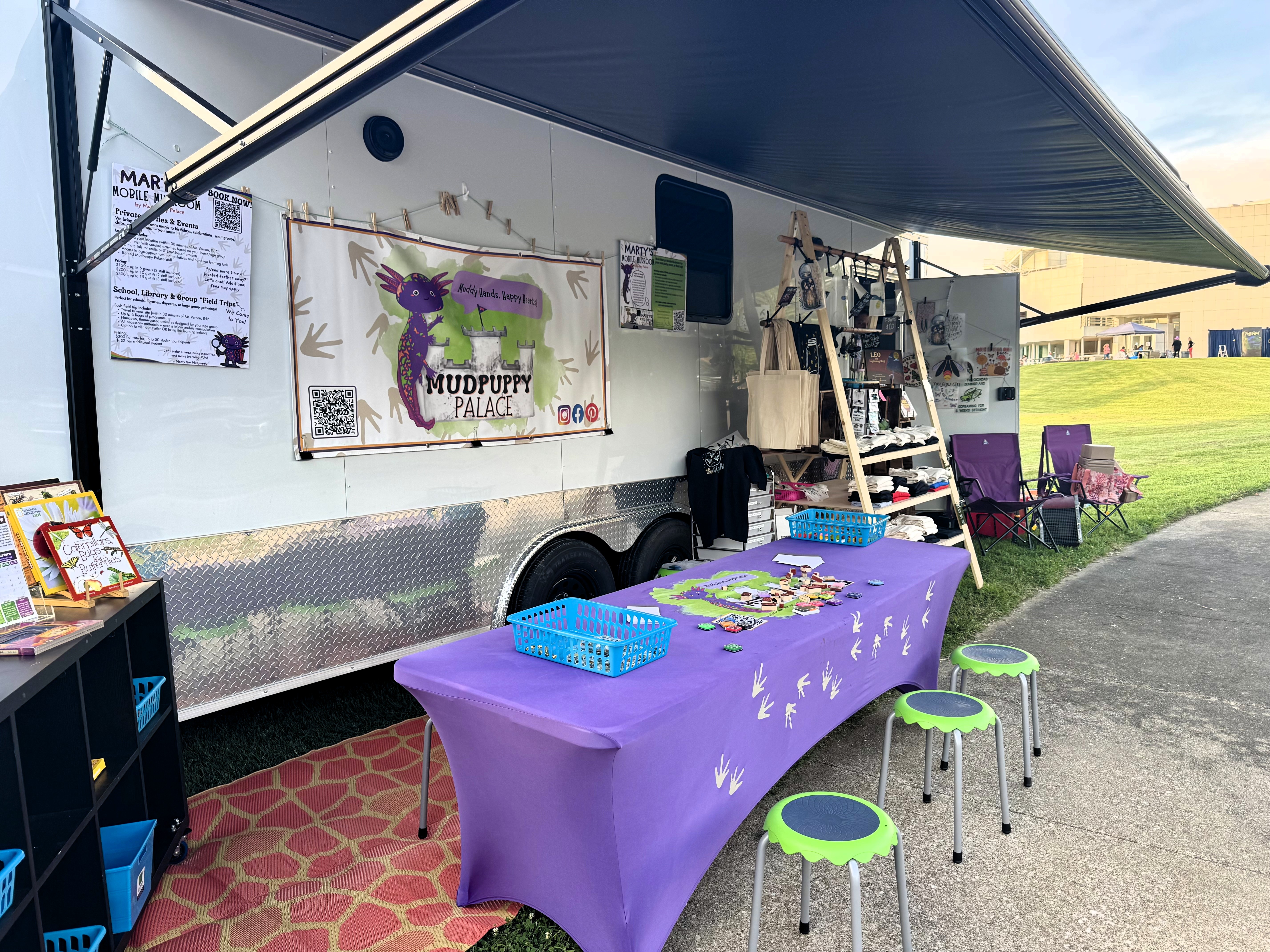 Vendor trailer with crafts and merchandise displayed on tables in front.