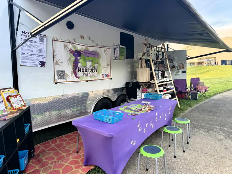 Vendor trailer with crafts and merchandise displayed on tables in front.