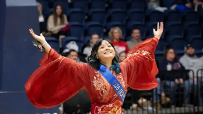 image of a student wearing a sash with their arms spread in Liberty Arena