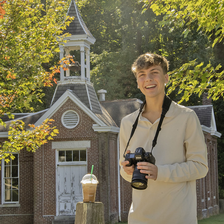 A photography student takes a break on a fall day in front of Schoolhouse No 3 at the Outdoor Education Center. 