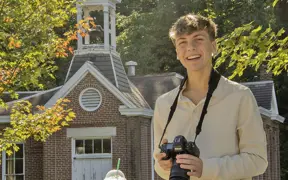 A photography student takes a break on a fall day in front of Schoolhouse No 3 at the Outdoor Education Center. 