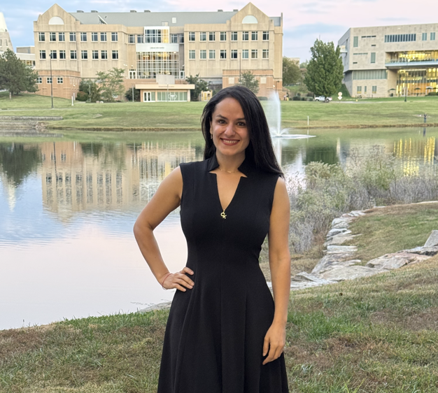 Hussein wears a black dress, posing in front of Reflection Lake on USI campus.