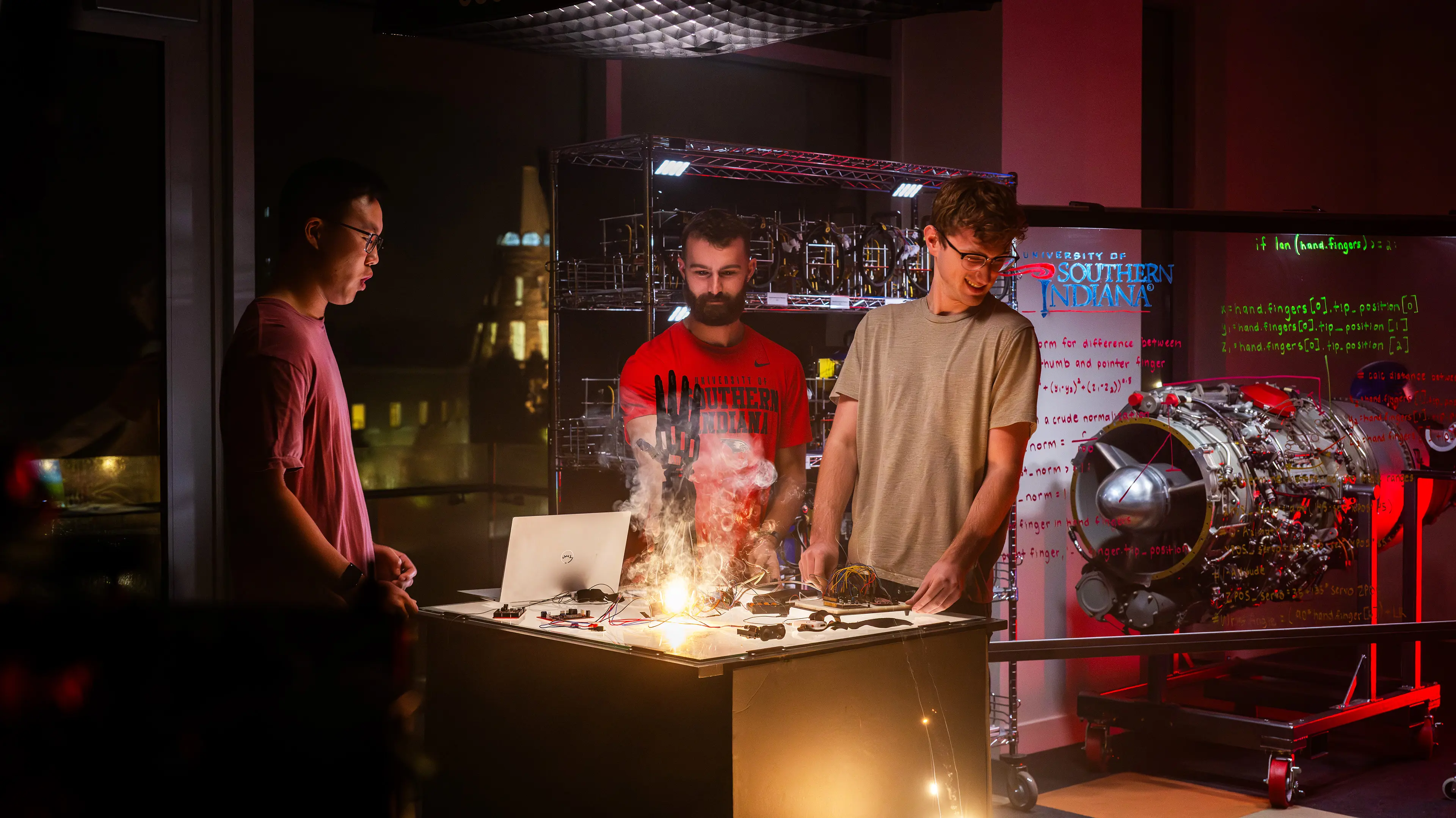 Late at night, USI students problem solve solutions for a prosthetic hand in an engineering lab with the cone in the background.