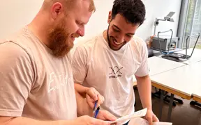Two smiling students looking at a paper during class