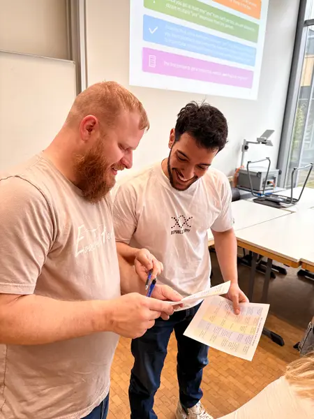 Two smiling students looking at a paper during class