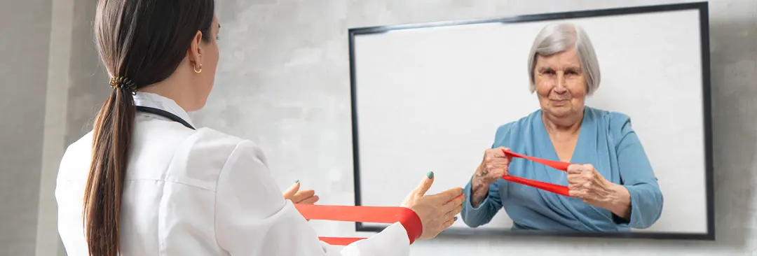 A healthcare professional demonstrating how to use a red exercise band via Telehealth to a patient displayed on a TV screen