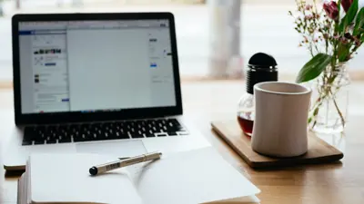 Open book next to laptop with coffee cup on side