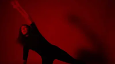 Woman does a full body stretch pose in a room lit by a red light