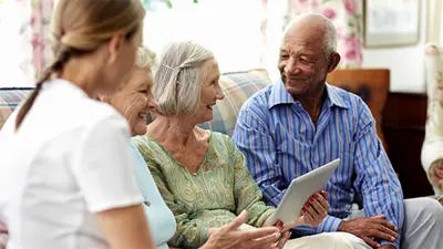 Healthcare provider with older adults holding a tablet on a couch