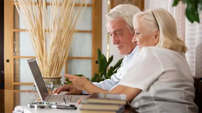 Two older adults smiling at a laptop