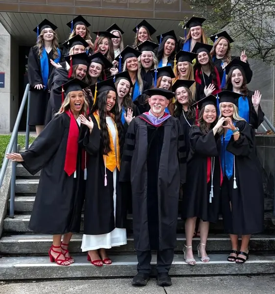 Students in caps and gowns pose with photo with Dr. Craig