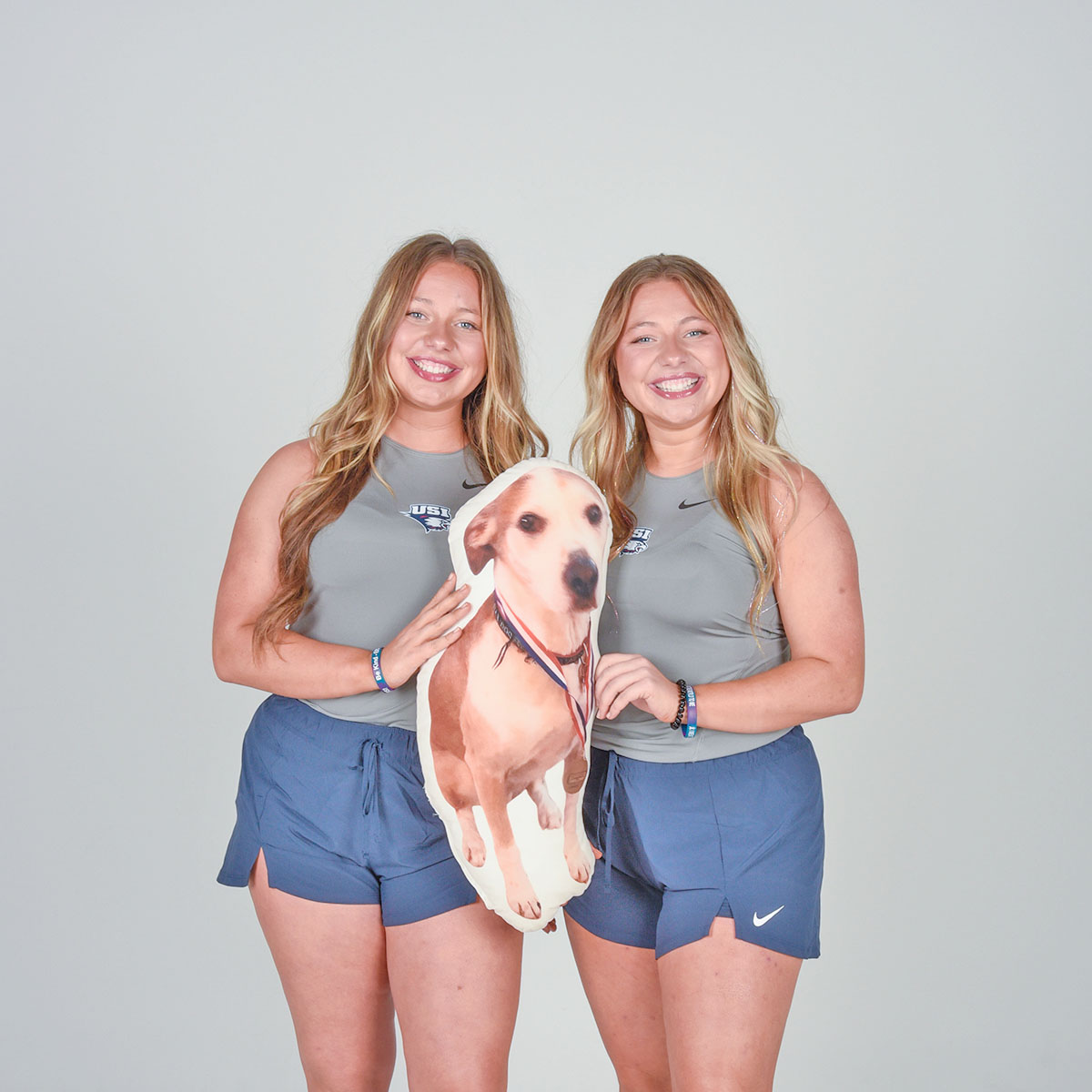 Twin members of USI's tennis team pose with a stuffed animal of their dog during the tennis media day in the photo studio.