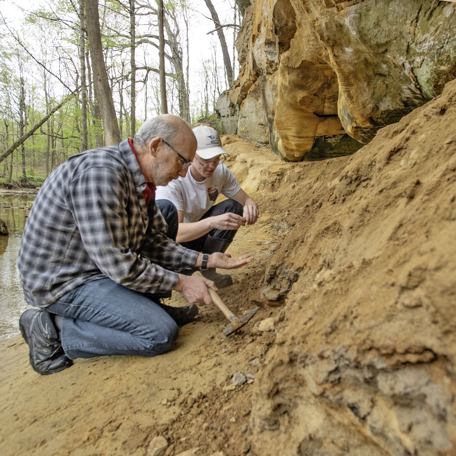professor and student examining rocks in front of a sandstone cliff