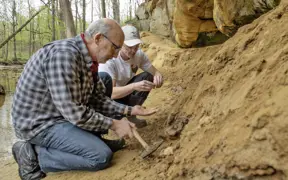 professor and student examining rocks in front of a sandstone cliff