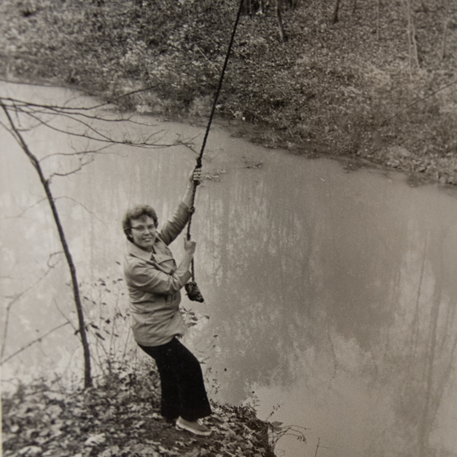 Doris Eicher, who spearheaded the trail and Outdoor Education Area development, playfully acts like she will swing on a rope at the edge of Reflection Lake