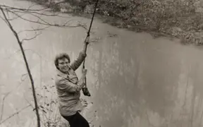 Doris Eicher, who spearheaded the trail and Outdoor Education Area development, playfully acts like she will swing on a rope at the edge of Reflection Lake
