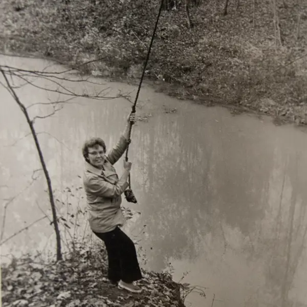 Doris Eicher, who spearheaded the trail and Outdoor Education Area development, playfully acts like she will swing on a rope at the edge of Reflection Lake