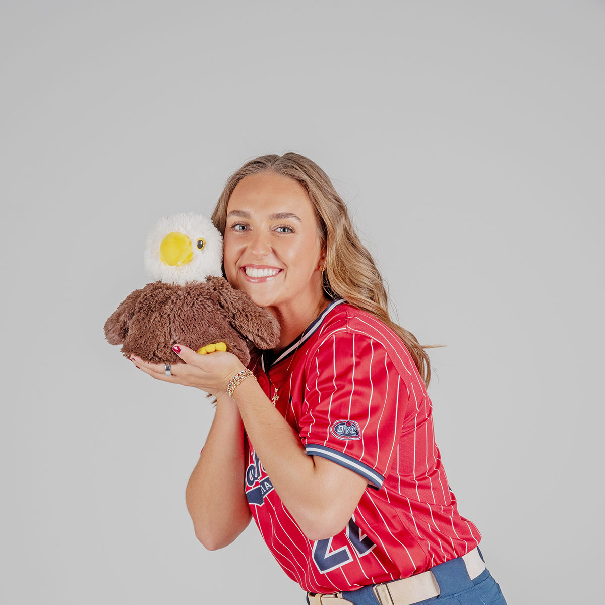 A women's softball player poses with a plush stuffed eagle for her media pose for softball media day in the photo studio.