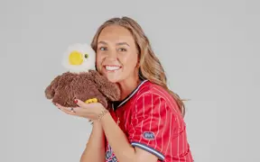 A women's softball player poses with a plush stuffed eagle for her media pose for softball media day in the photo studio.
