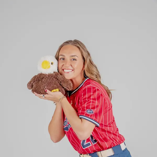 A women's softball player poses with a plush stuffed eagle for her media pose for softball media day in the photo studio.