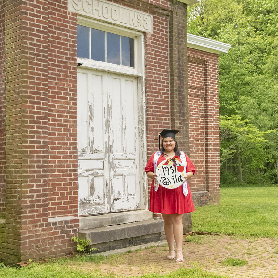Education graduate standing in front of the old schoolhouse located off the trails in the Outdoor Education Center. 