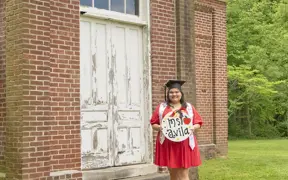 Education graduate standing in front of the old schoolhouse located off the trails in the Outdoor Education Center. 