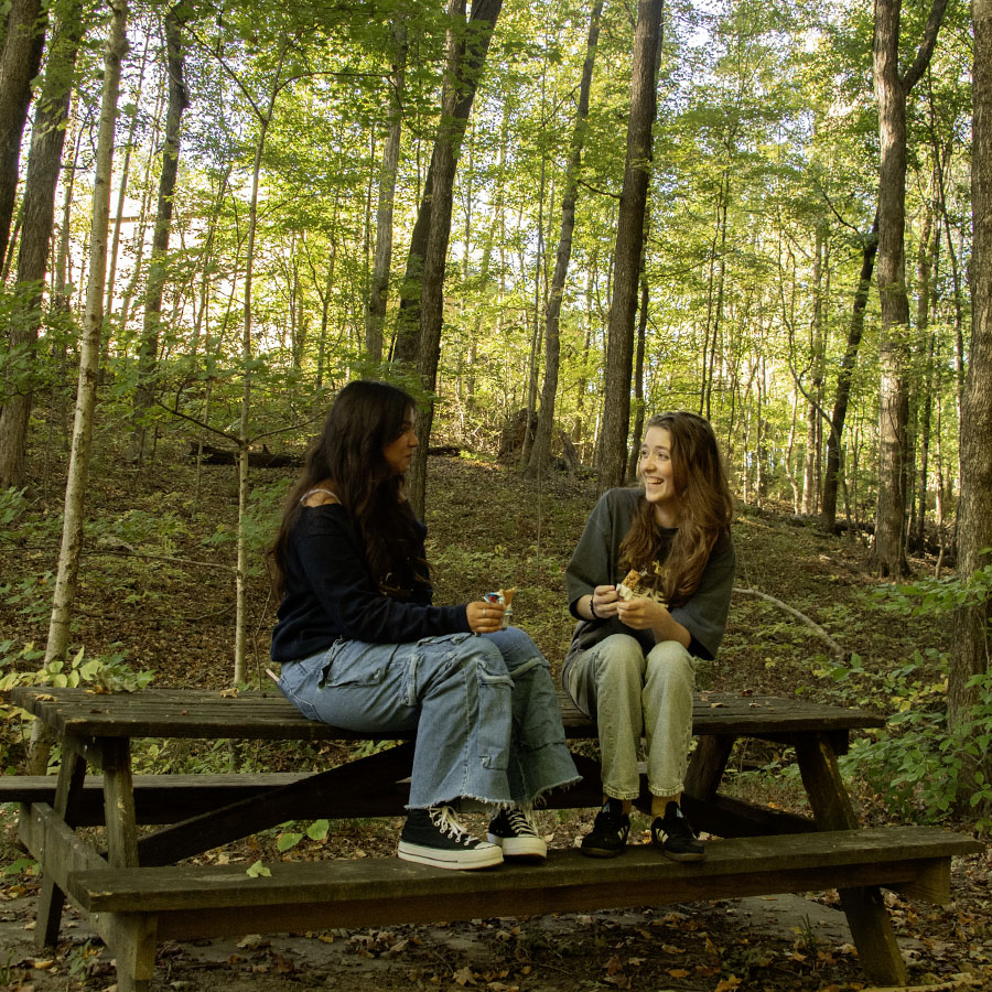Two students sit and talk on one of the three picnic tables found on the lakeside Oak Trail. 