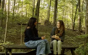 Two students sit and talk on one of the three picnic tables found on the lakeside Oak Trail. 