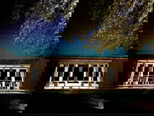 Photo shows a brick wall with a window looking out onto a dark field.