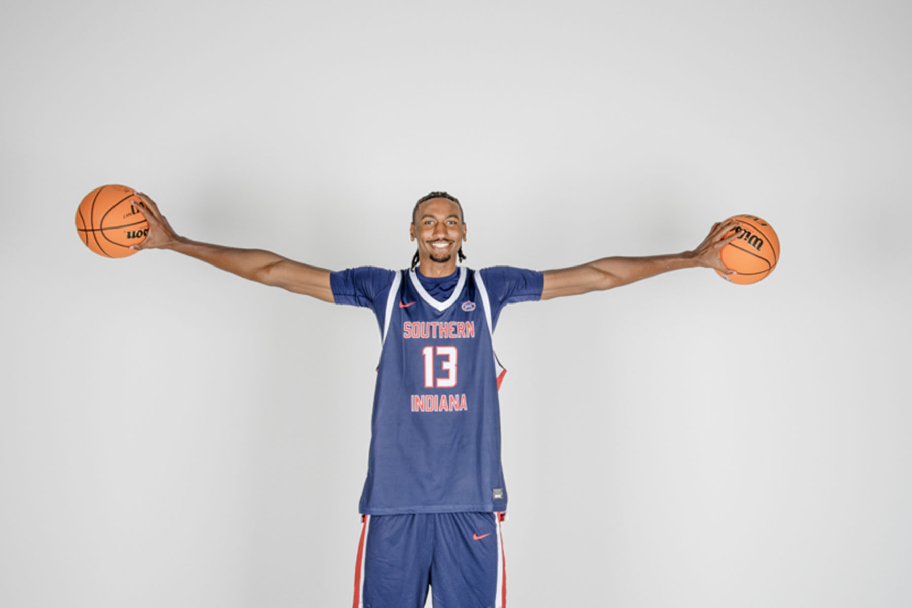 A basketball player palms basketballs in each hand as he holds his arms out to the side, displaying an impressive wing span at media day.