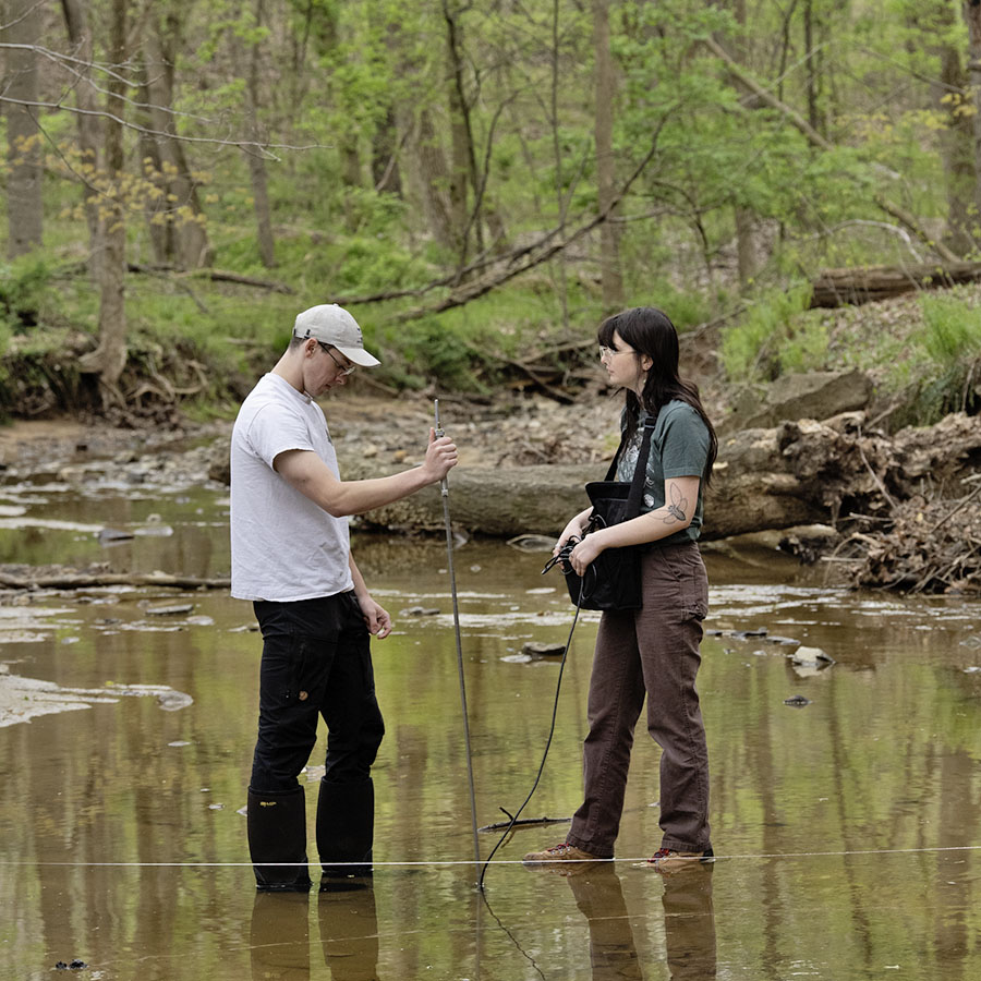 two students standing in a small creek, taking water measurements.