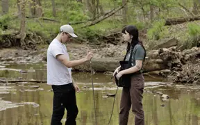 two students standing in a small creek, taking water measurements.
