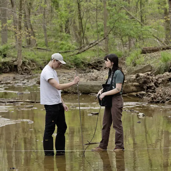 two students standing in a small creek, taking water measurements.