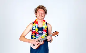 A smiling cross country runner wears two colorful leis and strums a ukulele for his media day photo.