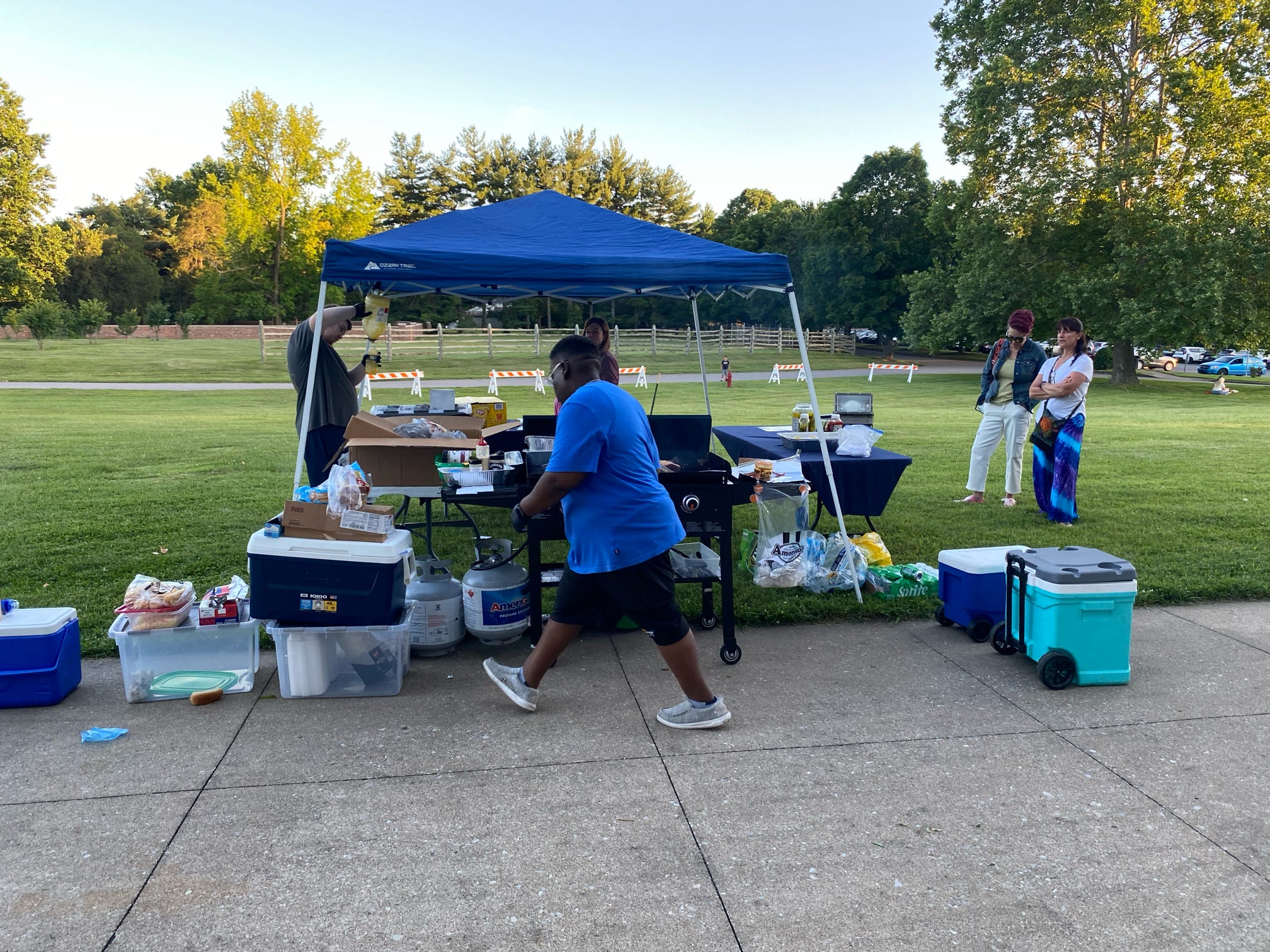 Outdoor refreshment station under a blue canopy with coolers and tables set up.