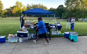 Outdoor refreshment station under a blue canopy with coolers and tables set up.