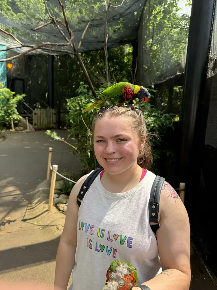 USI psychology graduate Keely Winkler '23 poses at the zoo with a small bird on her head