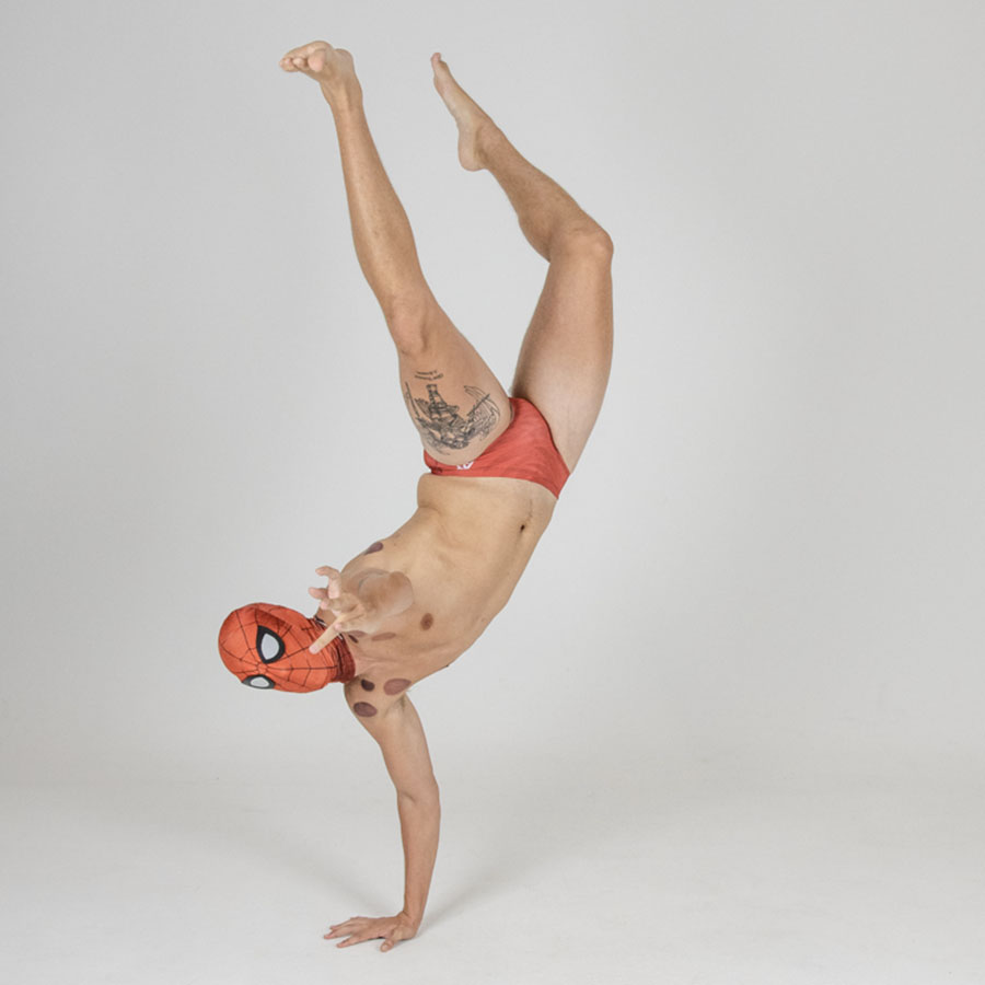 A swimmer, wearing a spiderman mask goes a one handed handstand-the other arm is outreached as he pretends to shoot webs at you.