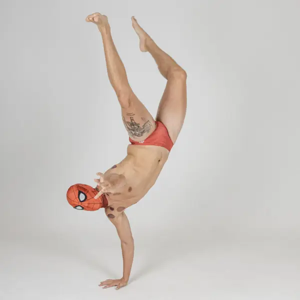 A swimmer, wearing a spiderman mask goes a one handed handstand-the other arm is outreached as he pretends to shoot webs at you.