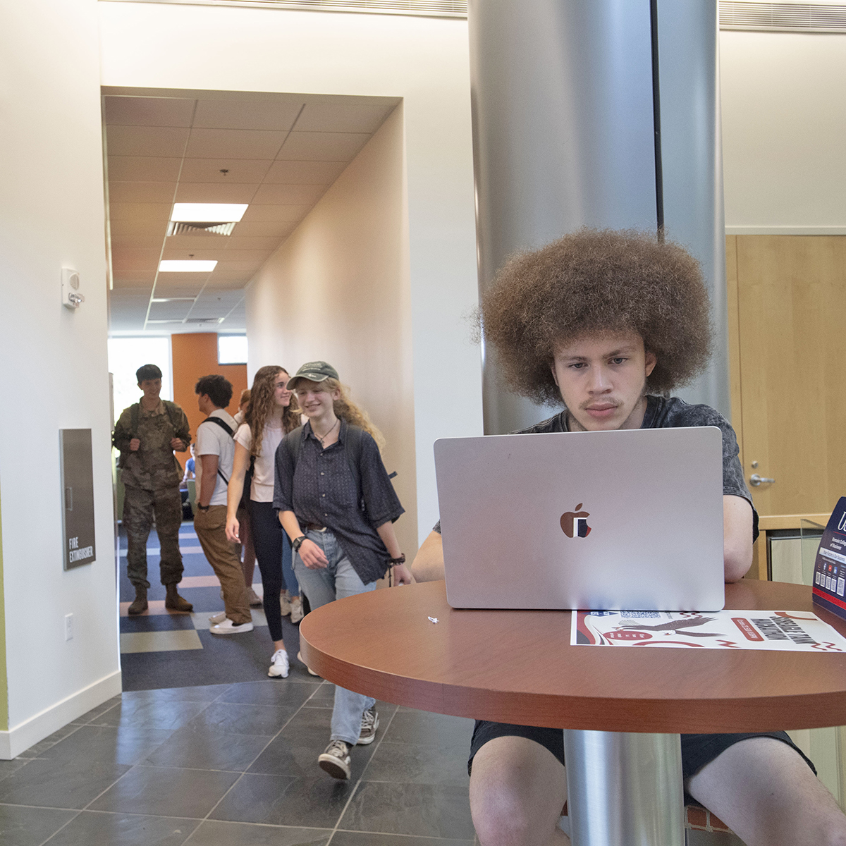Students pass by a student doing homework on a lap top at the Business Engineering Center.